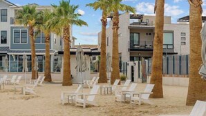 A beachfront property with multiple-story buildings, palm trees, and white lounge chairs on the sand. -  DesertColor St. George Spacious 4-bedroom house pool & hot tub front door steps (St. George)