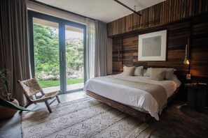 A modern bedroom with a large bed, a wooden headboard, a view through a sliding door, and a chair by the window. - VillaLaGrieta: Luxury Eco-Villa, Lagoon &Cenotes access, Ocean Views in Akumal (AKUMAL)