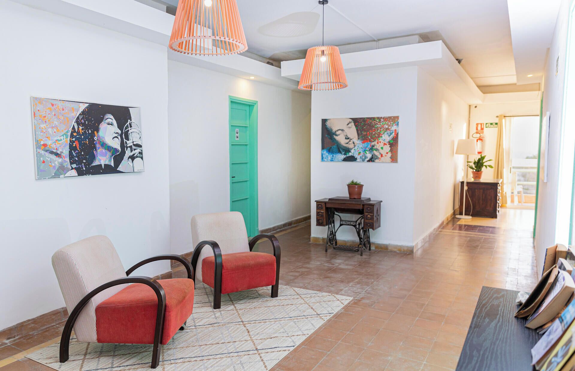 A hotel lobby with a seating area, artwork on the walls, a green door, and a desk with a plant.