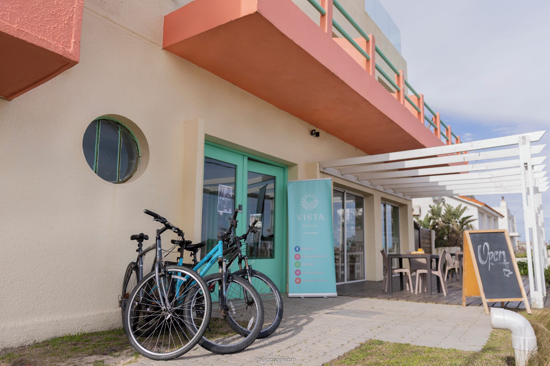 A hotel entrance with a teal door, bicycles parked outside, and a signboard with the hotel's name.