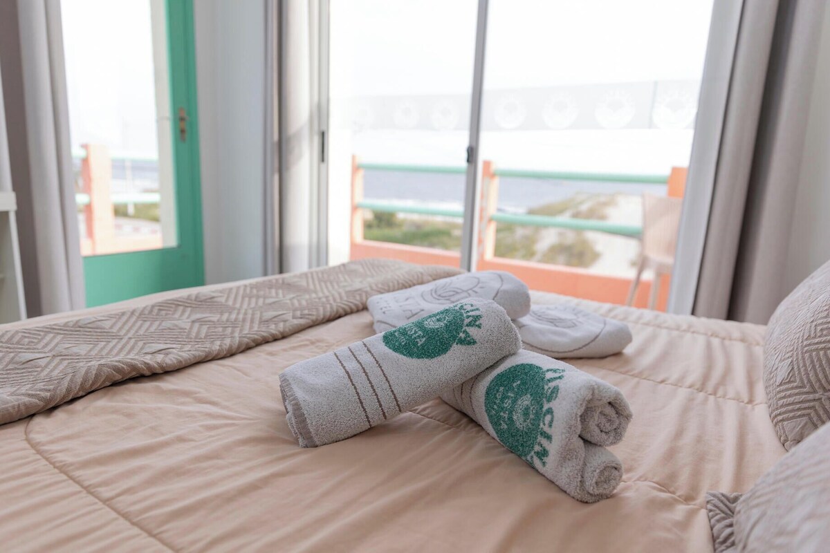 A hotel room with a bed, pillows, and a view of the sea through a balcony.
