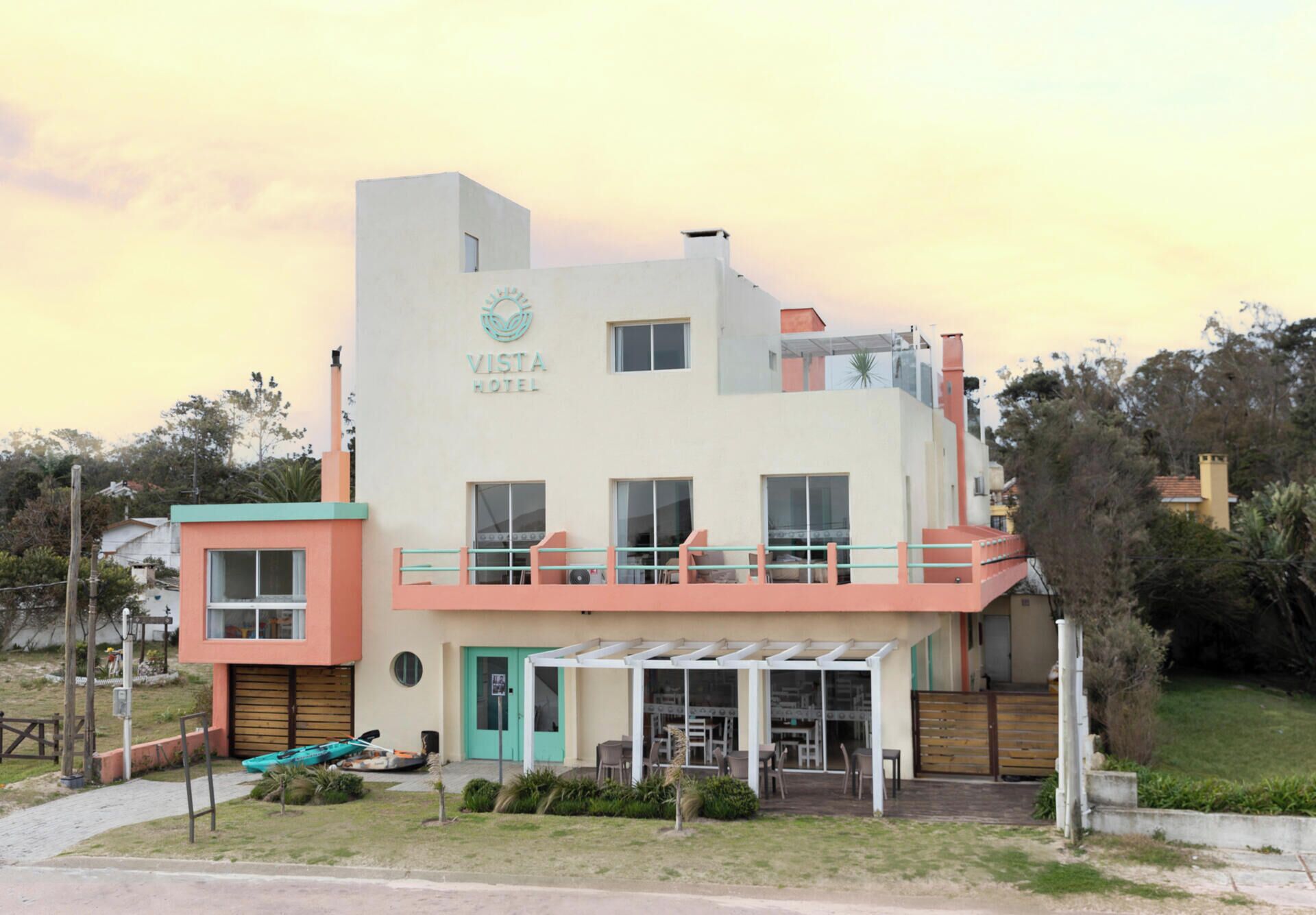 A two-story building with a sign reading 'Vista Hotel.' There is a covered outdoor seating area with tables and chairs.
