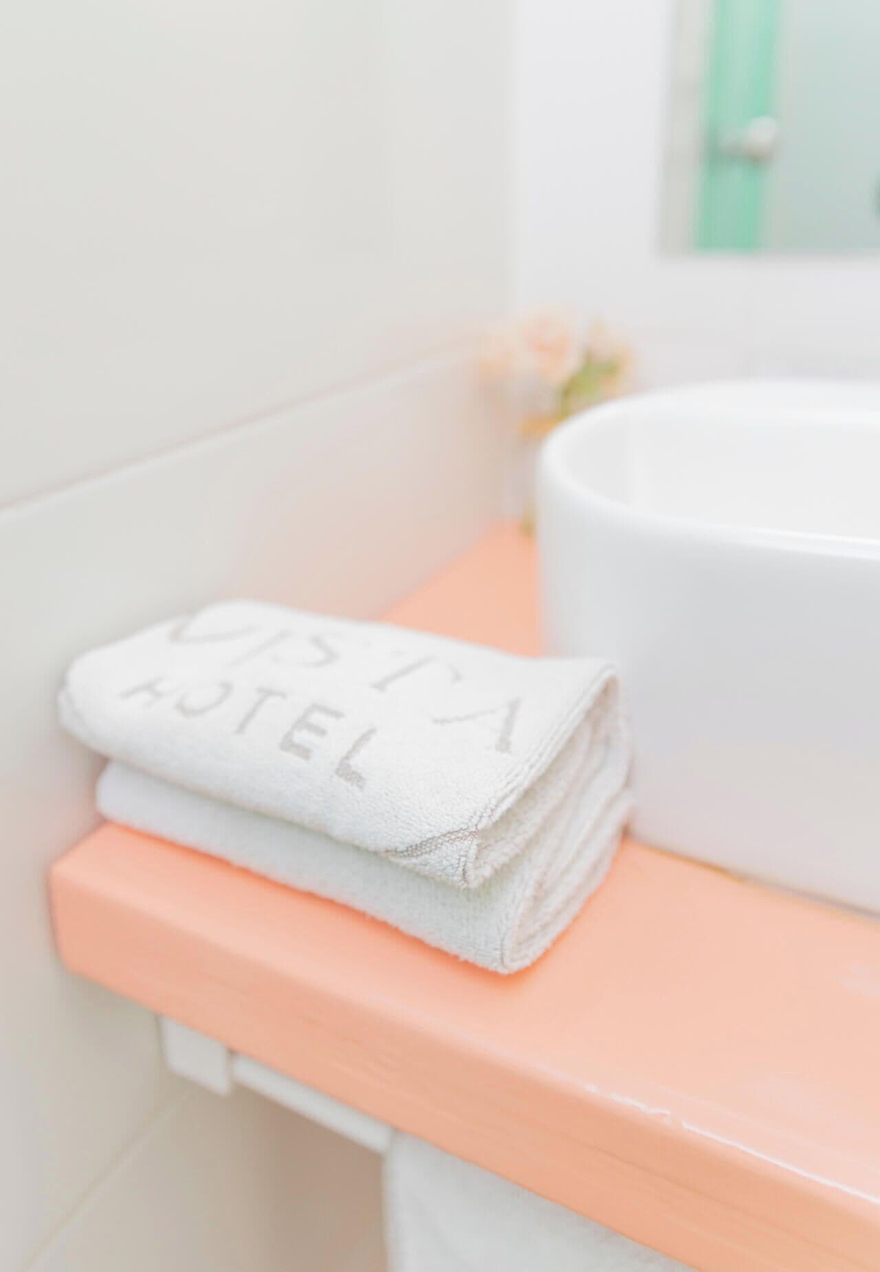 A bathroom with a white sink, a peach-colored countertop, and a folded white towel with text on it.