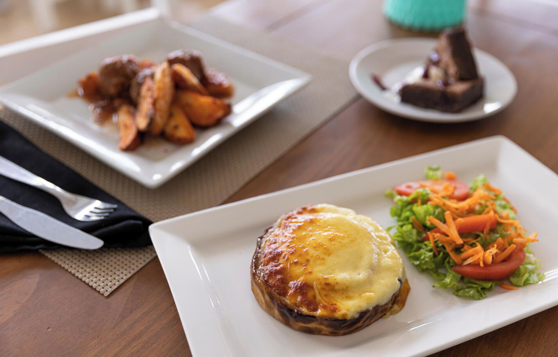A table with a plate of food consisting of a baked potato topped with cheese, a side salad, and a plate of meat.