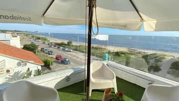 A balcony with a white umbrella, white plastic chairs, and a small table with a potted plant.