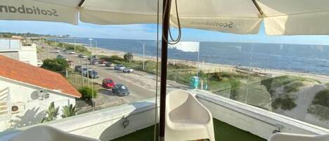 Un balcone con un ombrellone bianco, sedie in plastica bianca e un tavolino con una pianta in vaso.