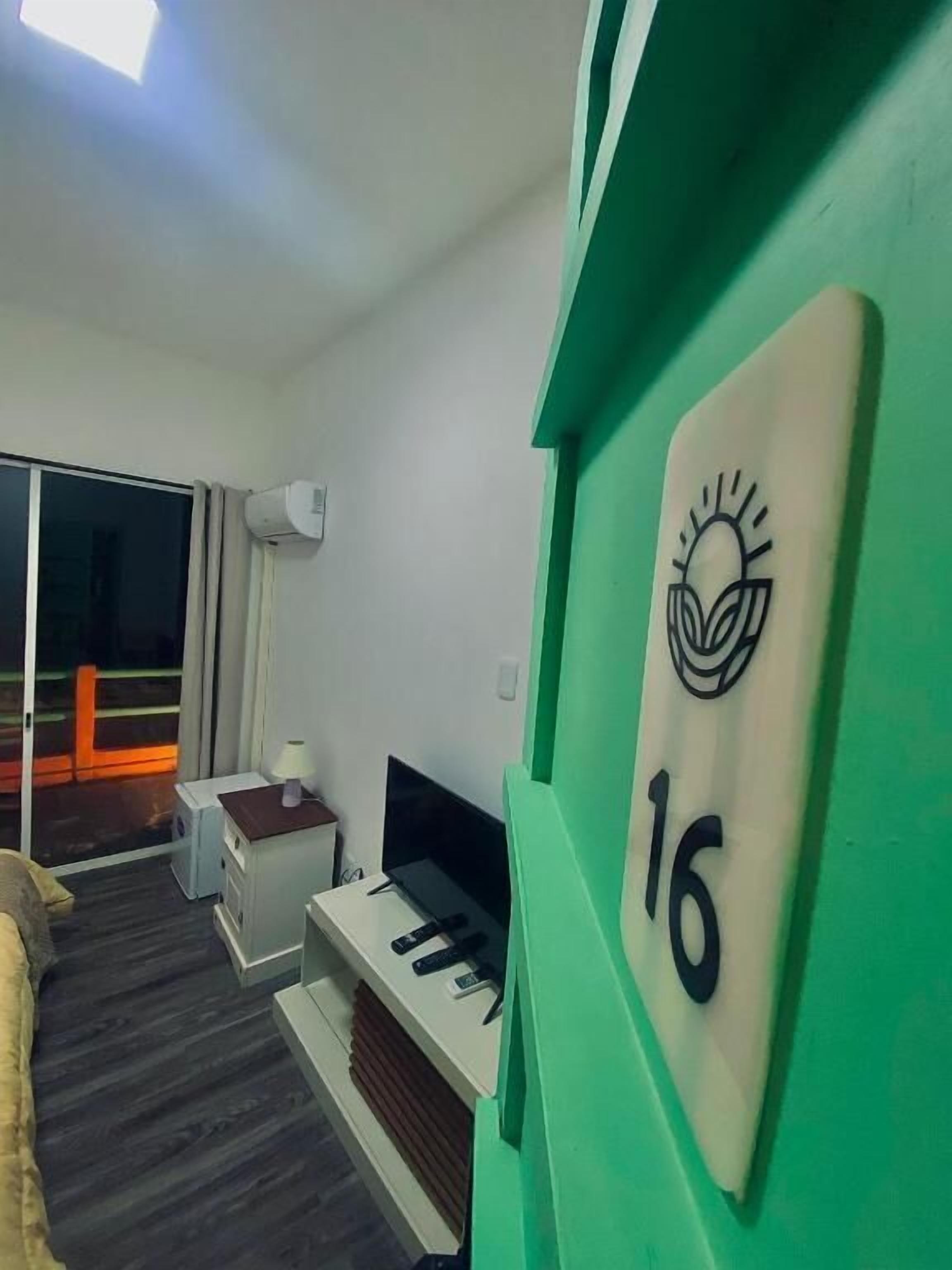 A room with a bed, a TV, a desk, and a green wall with a number sign.