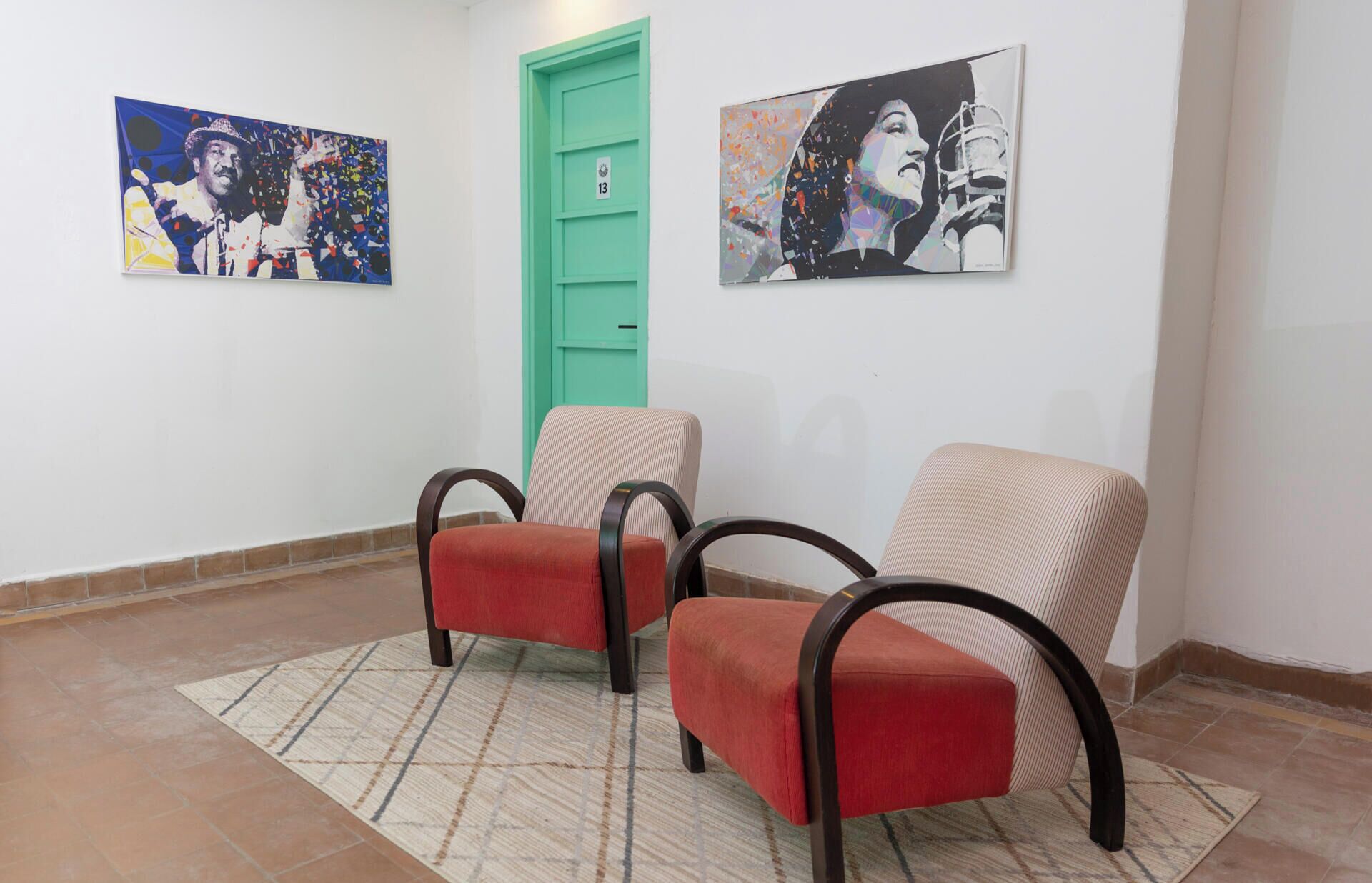 A lobby with two red armchairs, a green door, and two artworks on the walls.