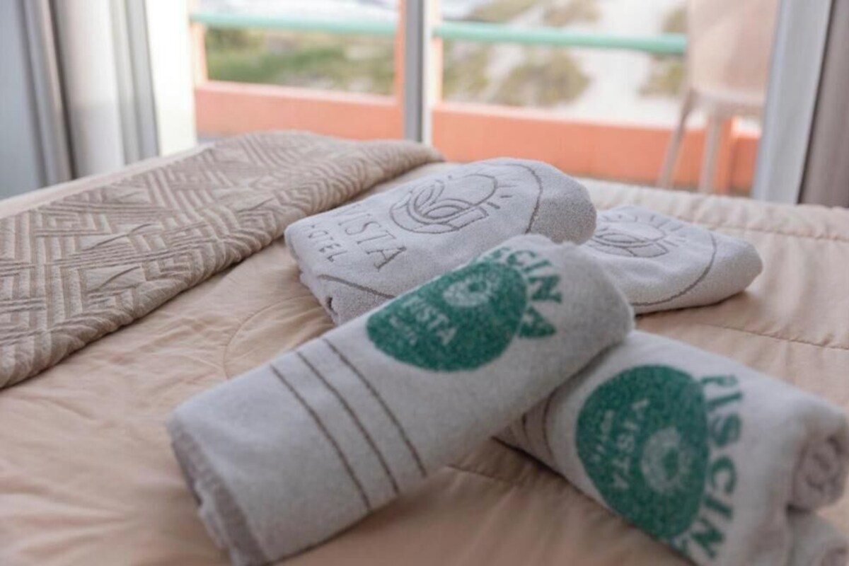 A bed with a patterned pillow and rolled towels with a logo.
