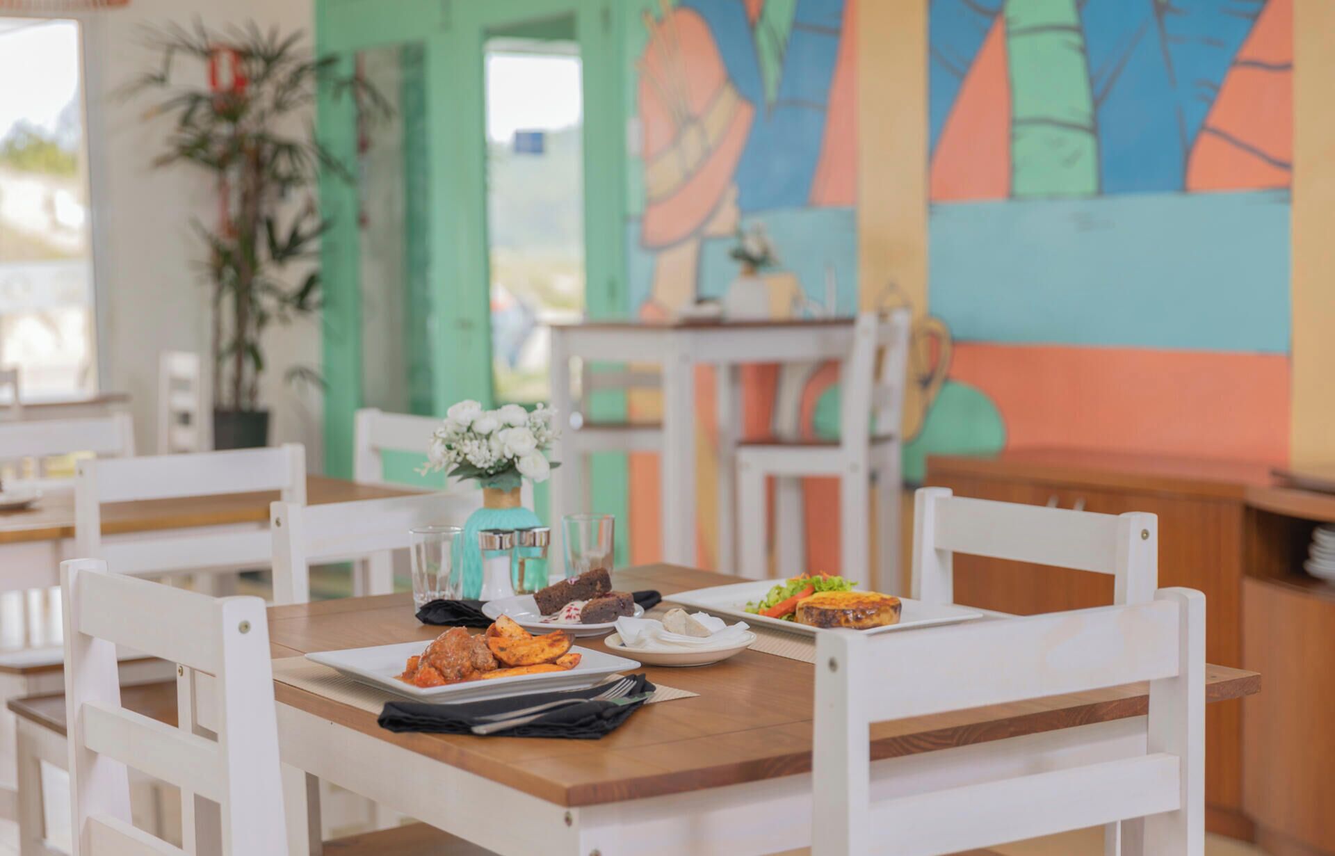 A dining area with white chairs, a wooden table, and a colorful abstract painting on the wall.