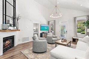 A modern living room with a fireplace, comfortable seating, a television, and a view of greenery outside. - Seagrove Gardens - Community Pool & 4 Bikes! (Santa Rosa Beach)
