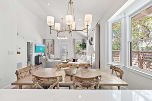 Ein geräumiger Essbereich mit Holztisch und Stühlen, einer Chandelier und großen Fenstern mit Blick ins Freie.