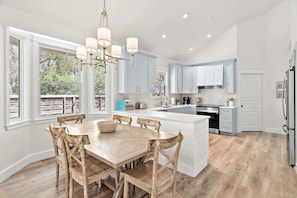A modern kitchen with a large island, wooden chairs, and a chandelier. - Seagrove Gardens - Community Pool & 4 Bikes! (Santa Rosa Beach)