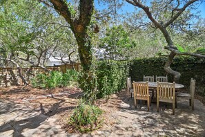 An outdoor patio with a wooden table and chairs, surrounded by trees and a stone wall. - Seagrove Gardens - Community Pool & 4 Bikes! (Santa Rosa Beach)