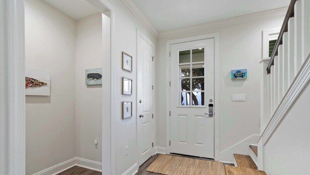 A hallway with a wooden floor, white walls, a white door with glass panels, and a small rug at the entrance. - Pet-Friendly 30A Cottage w/ Fenced Yard! (Santa Rosa Beach)