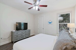 Ein Schlafzimmer mit einem Bett, einem Fernseher auf einer Kommode, einem Deckenventilator und einem Fenster mit Jalousien.