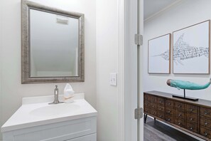 Ein Badezimmer mit weißem Waschtisch, einem Spiegel mit dekorativem Rahmen, einem Handtuchspender und einem Schrank mit Schubladen.