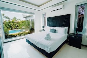 A modern bedroom with a large bed, a view of a swimming pool, and a balcony. - Casa Bonita Aruba | 4-Bedroom Villa with Private Pool (Oranjestad)