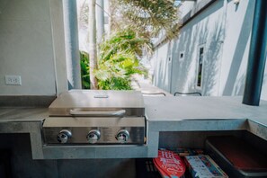 A kitchen with a built-in grill, a window overlooking a garden, and a countertop with a magazine. - Casa Bonita Aruba | 4-Bedroom Villa with Private Pool (Oranjestad)
