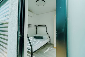 A single bed with a metal frame, white bedding, and a dark green blanket. - Casa Bonita Aruba | 4-Bedroom Villa with Private Pool (Oranjestad)