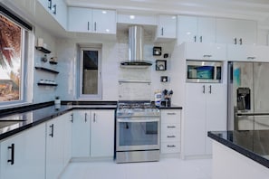 A modern kitchen with white cabinets, stainless steel appliances, and black countertops. - Casa Bonita Aruba | 4-Bedroom Villa with Private Pool (Oranjestad)