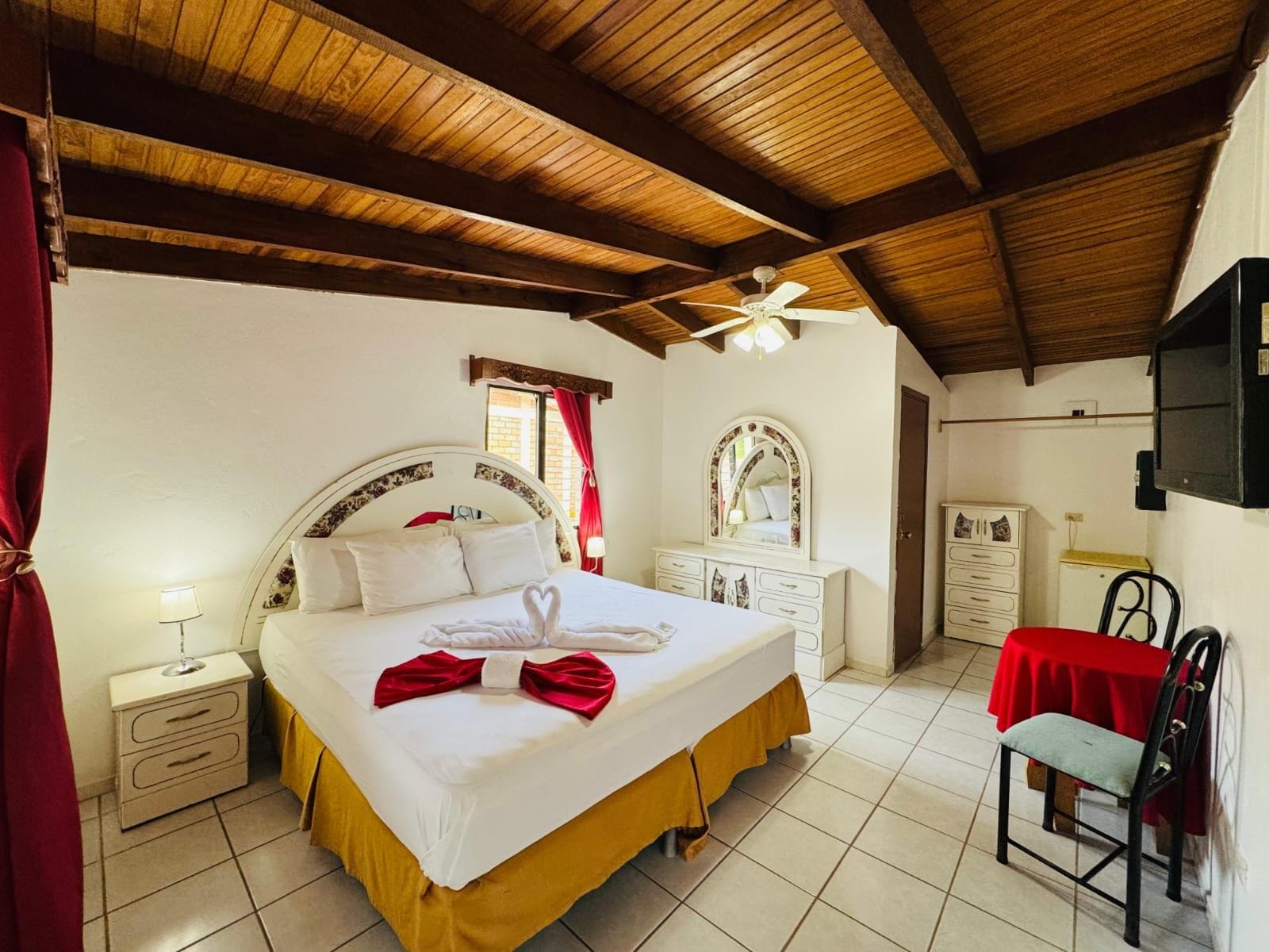 Una habitación de hotel con cama, mesitas de noche, armario, escritorio con silla y ventilador de techo.