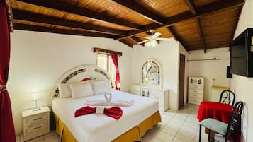 Una habitación de hotel con cama, mesitas de noche, armario, escritorio con silla y ventilador de techo.
