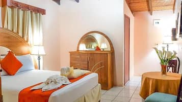 A bedroom with a bed, a wooden dresser, a mirror, a round table, and a chair.