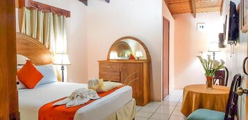 A bedroom with a bed, a wooden dresser, a mirror, a round table, and a chair.