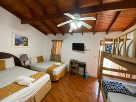 Una habitación con dos camas, un escritorio, un ventilador de techo y una televisión.