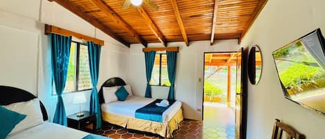 Habitación de hotel con techo de madera, cama con ropa de cama azul, televisor en la pared y vistas a zonas verdes.