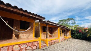 Un edificio con base de piedra y paredes pintadas de amarillo, que cuenta con un porche y una hamaca.