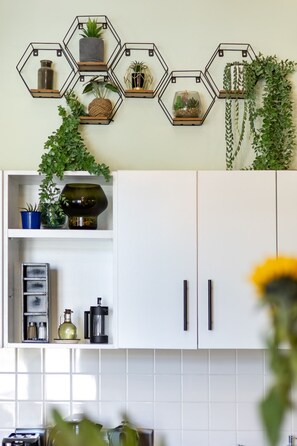 Uma cozinha com armários brancos, um painel hexagonal de plantas na parede e uma janela com vista para o exterior.