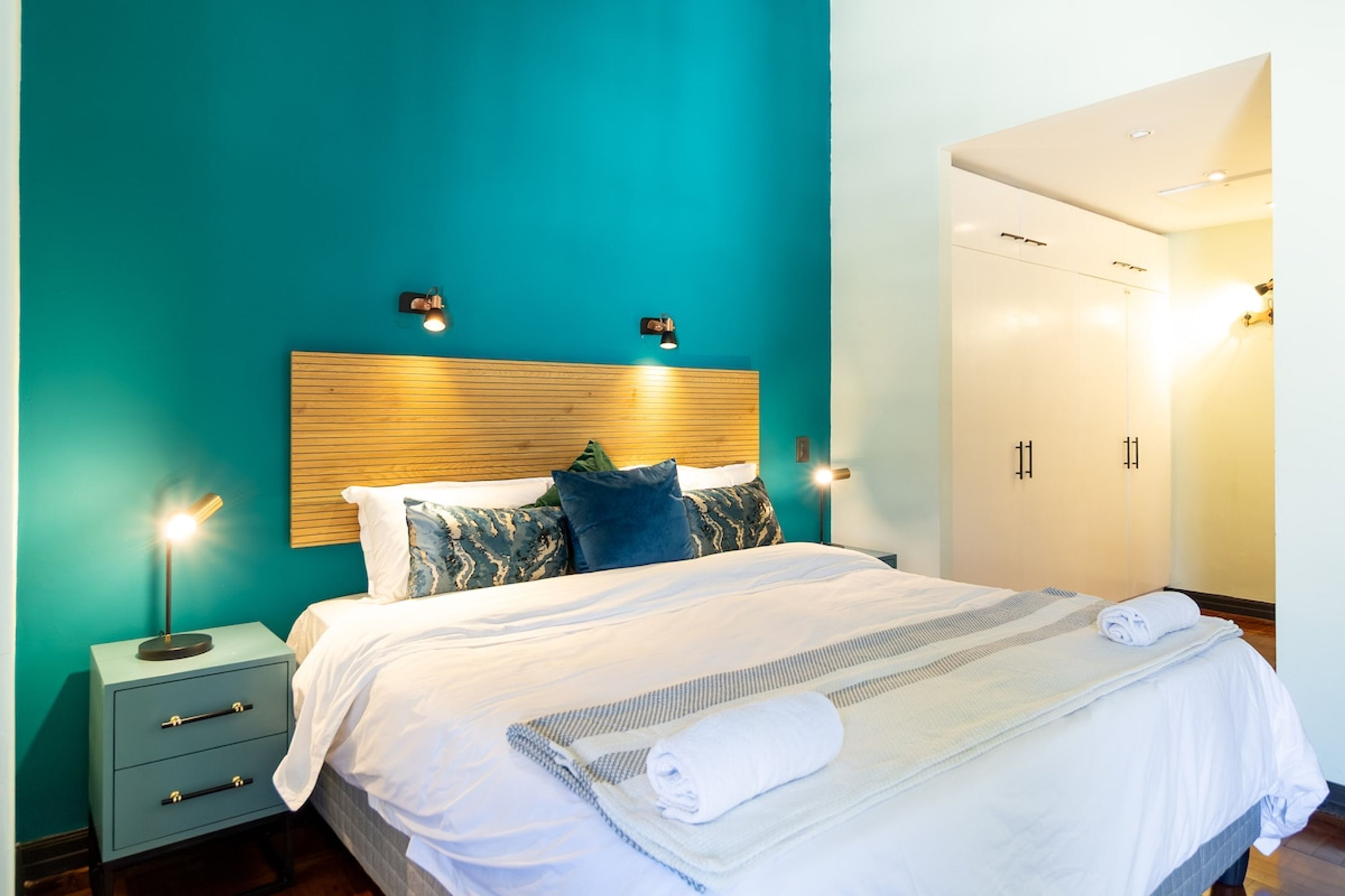 A hotel room with a bed, bedside tables, a wardrobe, and wall-mounted lights.