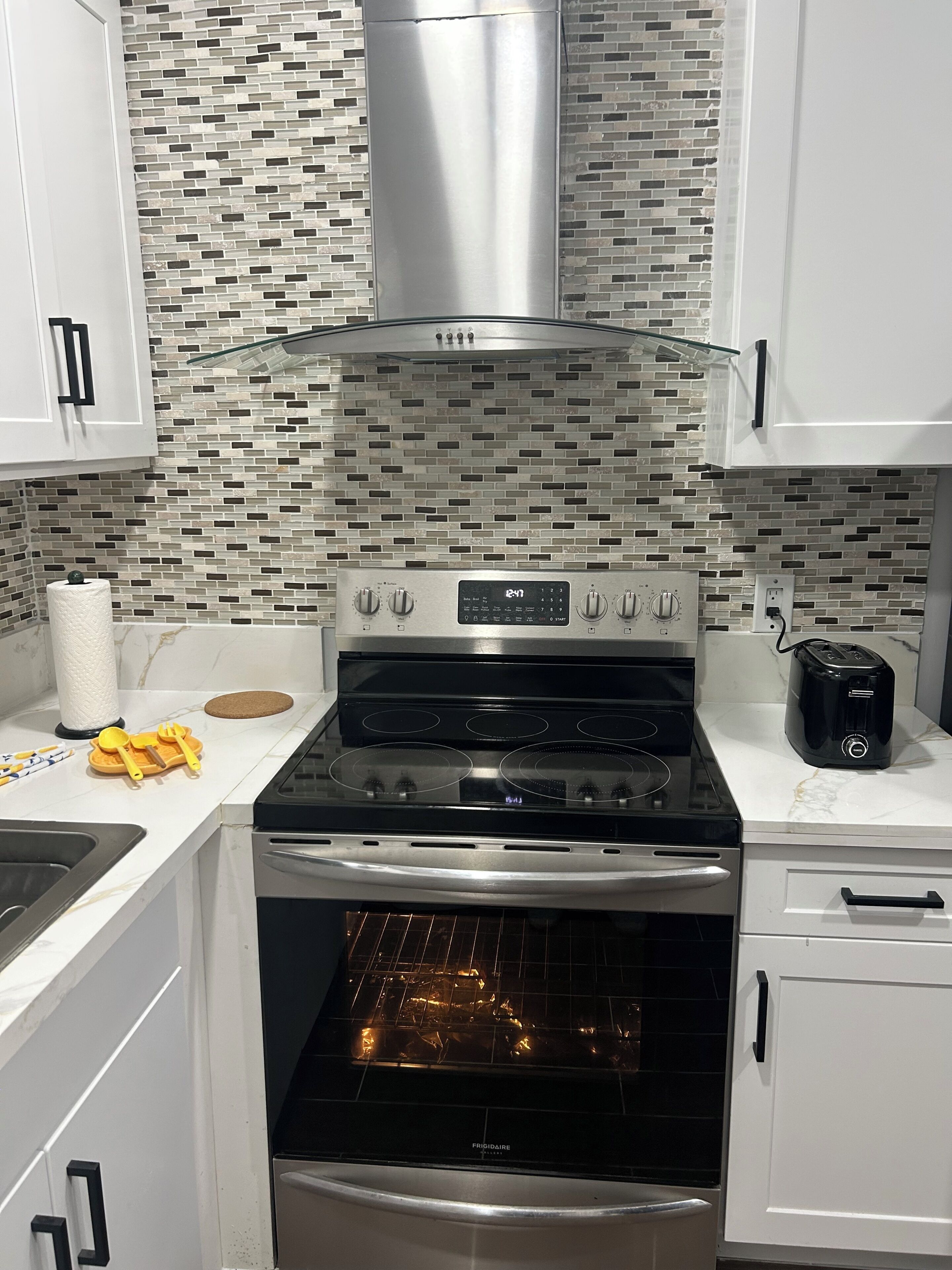 A kitchen with a stainless steel range hood, a built-in oven, and a tiled backsplash.