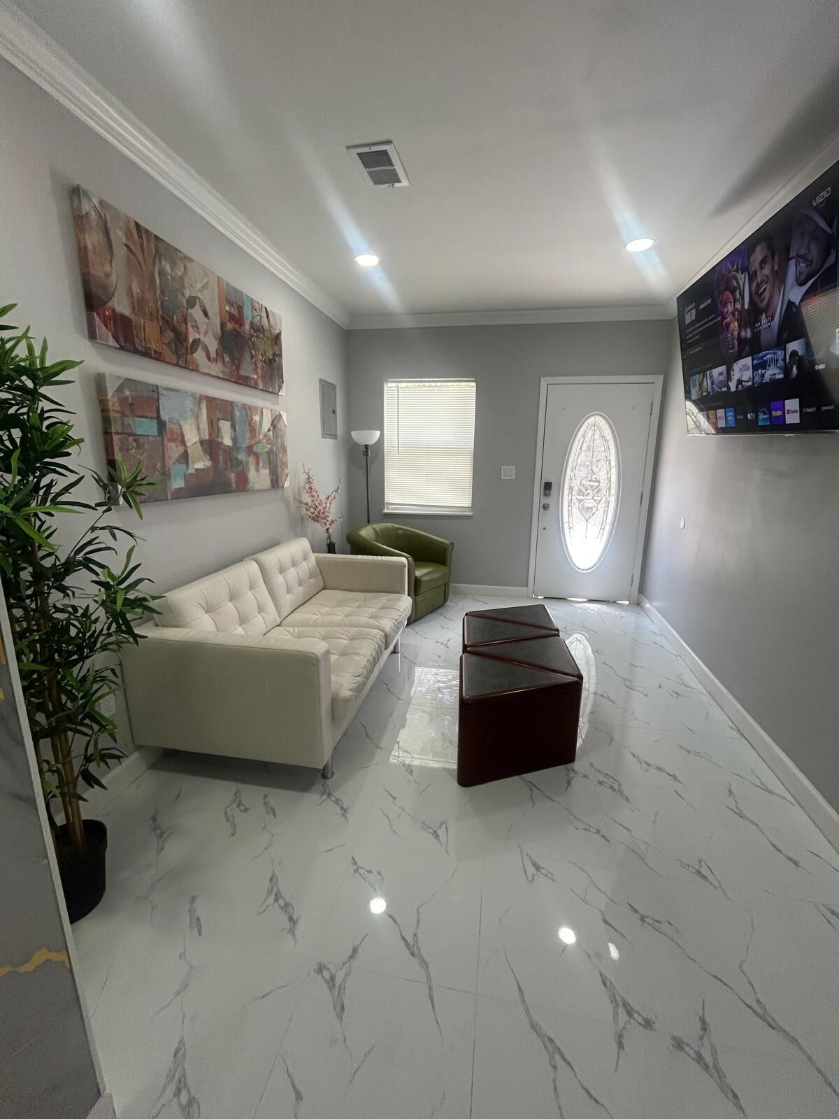 A modern living room with a white sofa, a coffee table, and a TV on the wall.