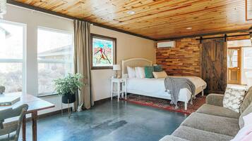Ein Zimmer mit einem Bett, einem Schreibtisch, einem Sessel, einer Pflanze und einem Fenster mit Vorhängen.