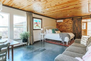A room with a bed, a desk, a chair, a plant, and a window with curtains.