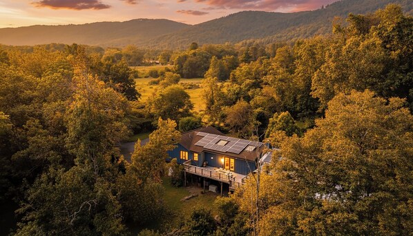 A house with a solar panel roof surrounded by dense forest and hills.