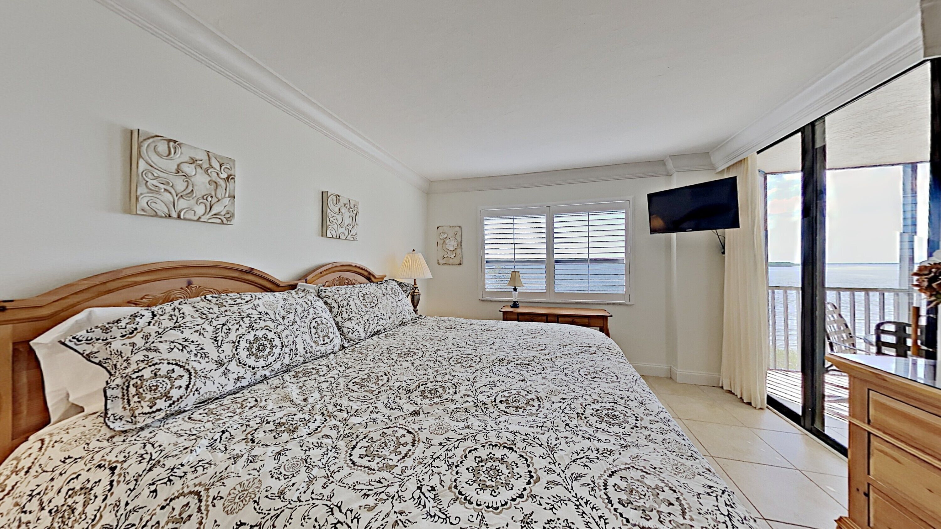 A bedroom with a large bed, a television, and a window with blinds.