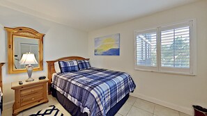 A bedroom with a bed, a nightstand, a lamp, a painting, and a window. - 2-bedroom Beach-front apartment in Punta Russa (Fort Myers)