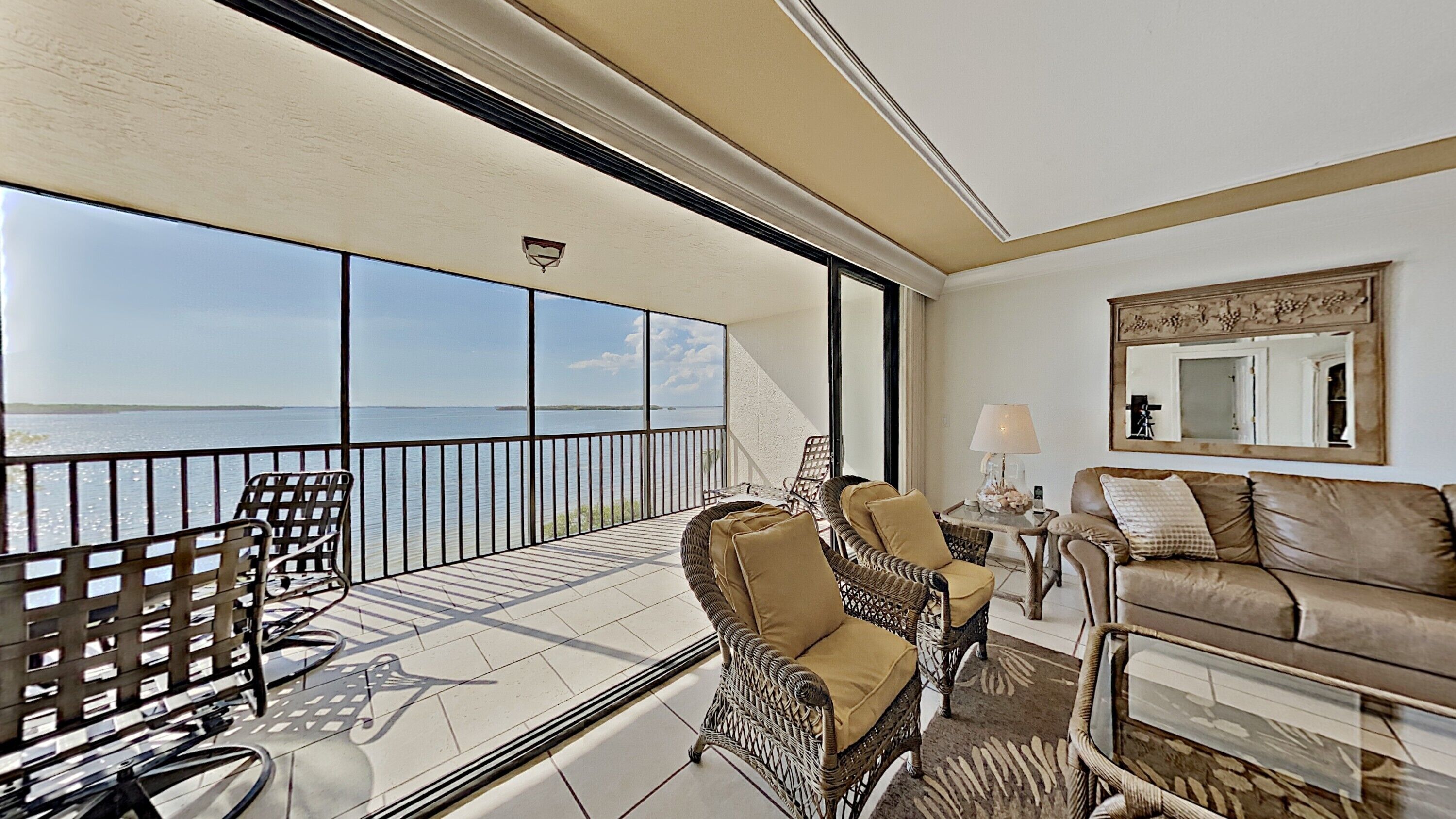 A balcony with a view of the sea, wicker furniture, a leather sofa, and a mirror.