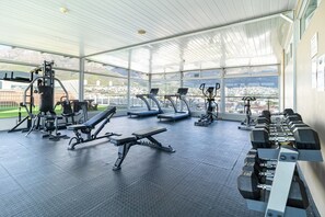 A gym with various exercise equipment, a bench, and a view of a cityscape through large windows. - Elevé Cape Town | Exclusive Panorama Suite (Cape Town)