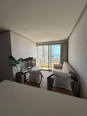 A modern living room with a sofa, a dining table, and a large window with a view of high-rise buildings. - 3 bedrooms | Private balcony, 5 min. from the beach (Cartagena de Indias)