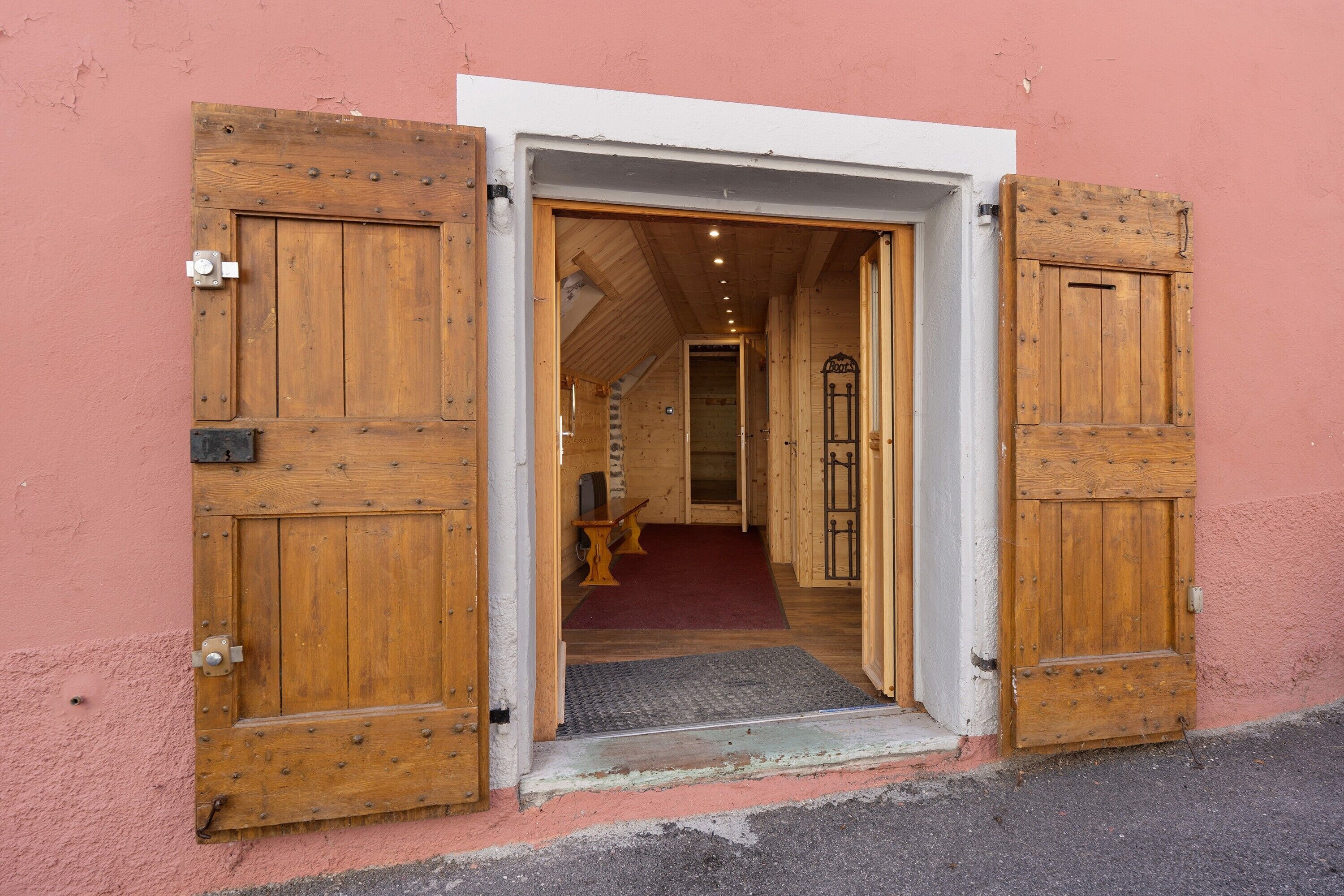 Une porte en bois avec un loquet métallique, qui donne sur une pièce dotée d’une moquette rouge et d’un banc.