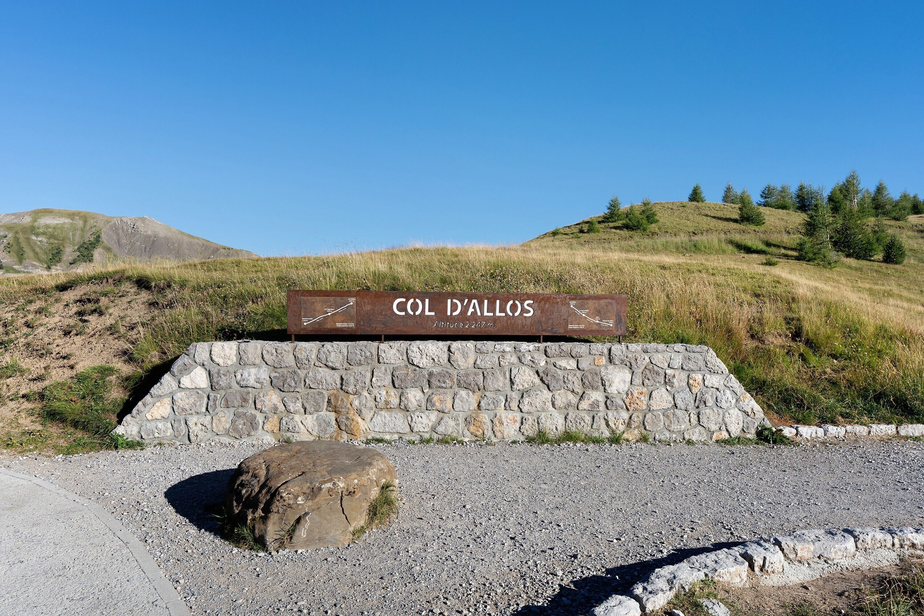 A sign with the text 'COL D'ALLOS' and a stone wall with a large rock in front.