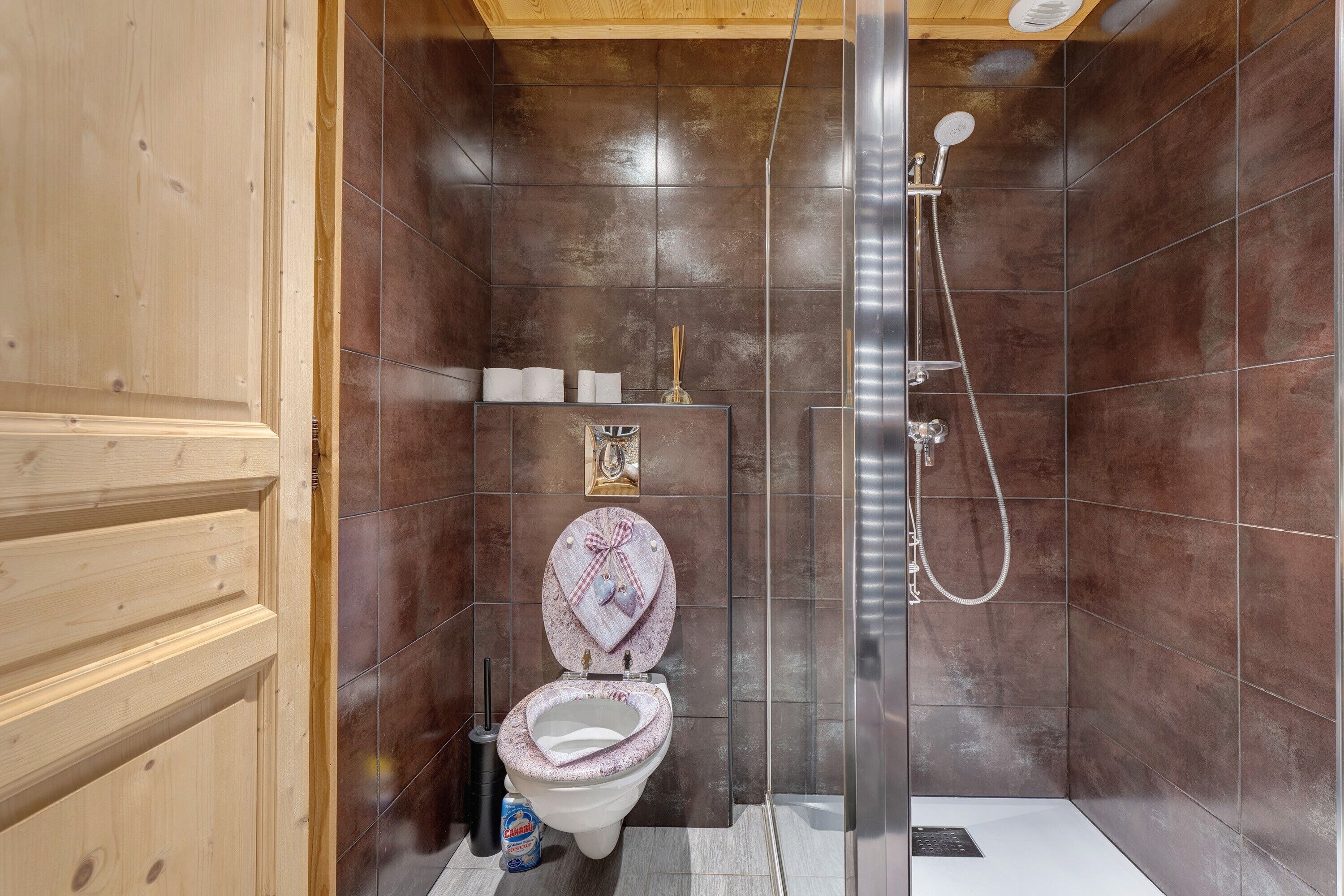 A small, compact bathroom with a shower, a toilet, and a shelf with toiletries.