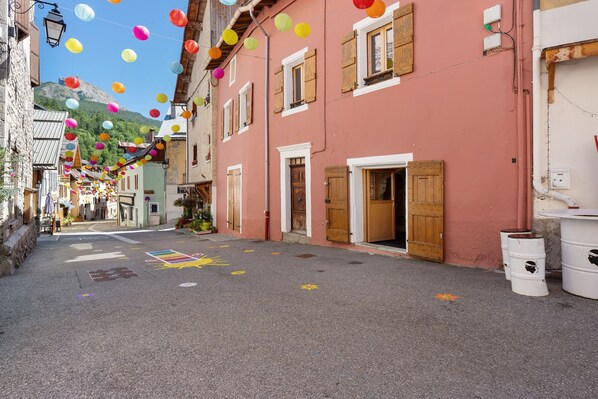 Una calle con faroles de papel de colores, contraventanas de madera y un edificio de fachada rosa.