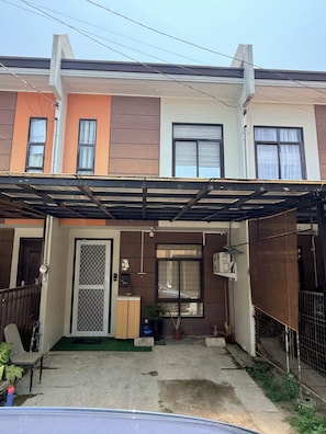 En bostadsbyggnad med en täckt uteplats, en grind vid ingången och en liten trädgårdsyta.