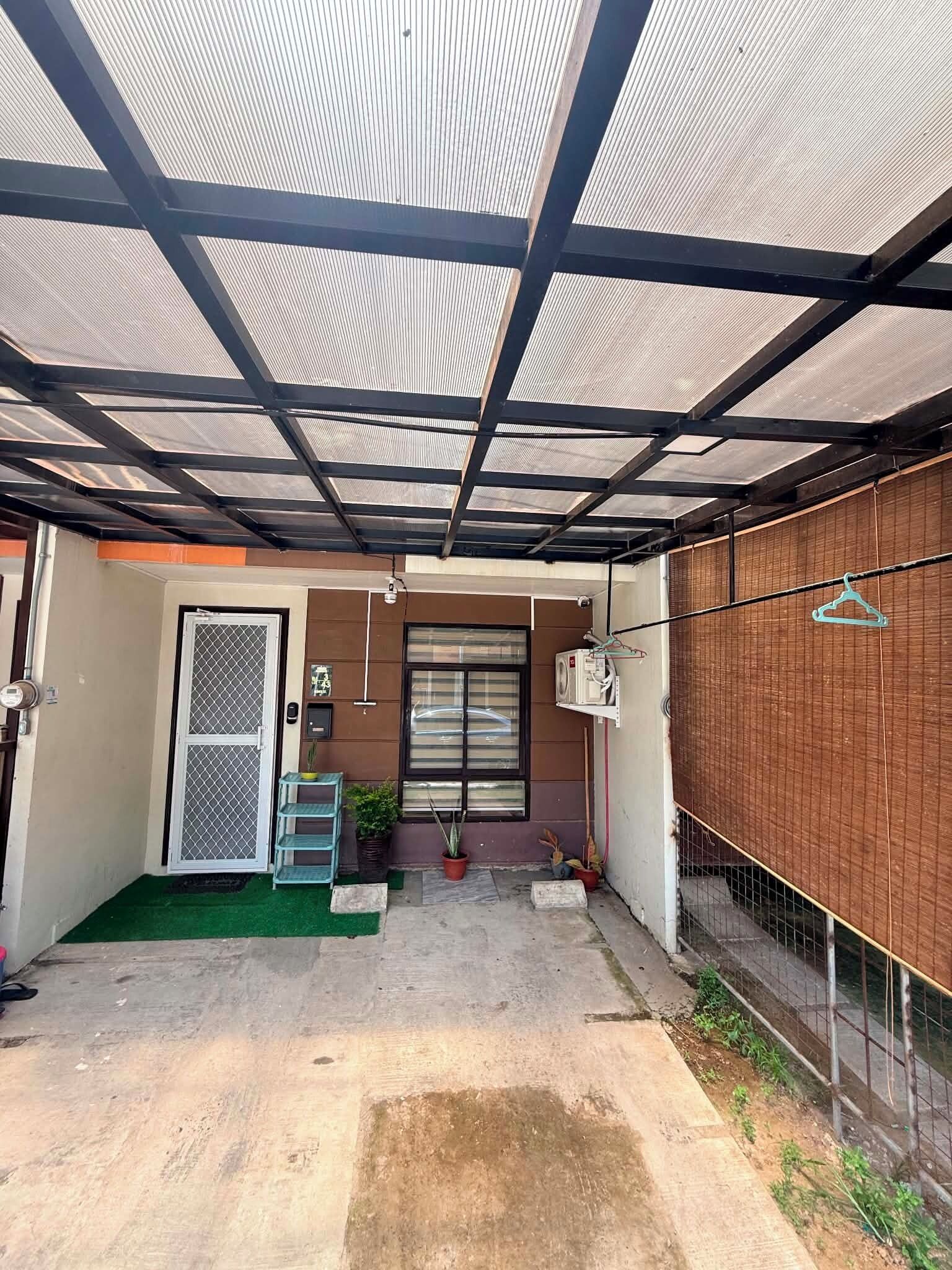 A covered outdoor area with a metal roof, a door with a security screen, a window, and a wall with a hanging clothes rack.